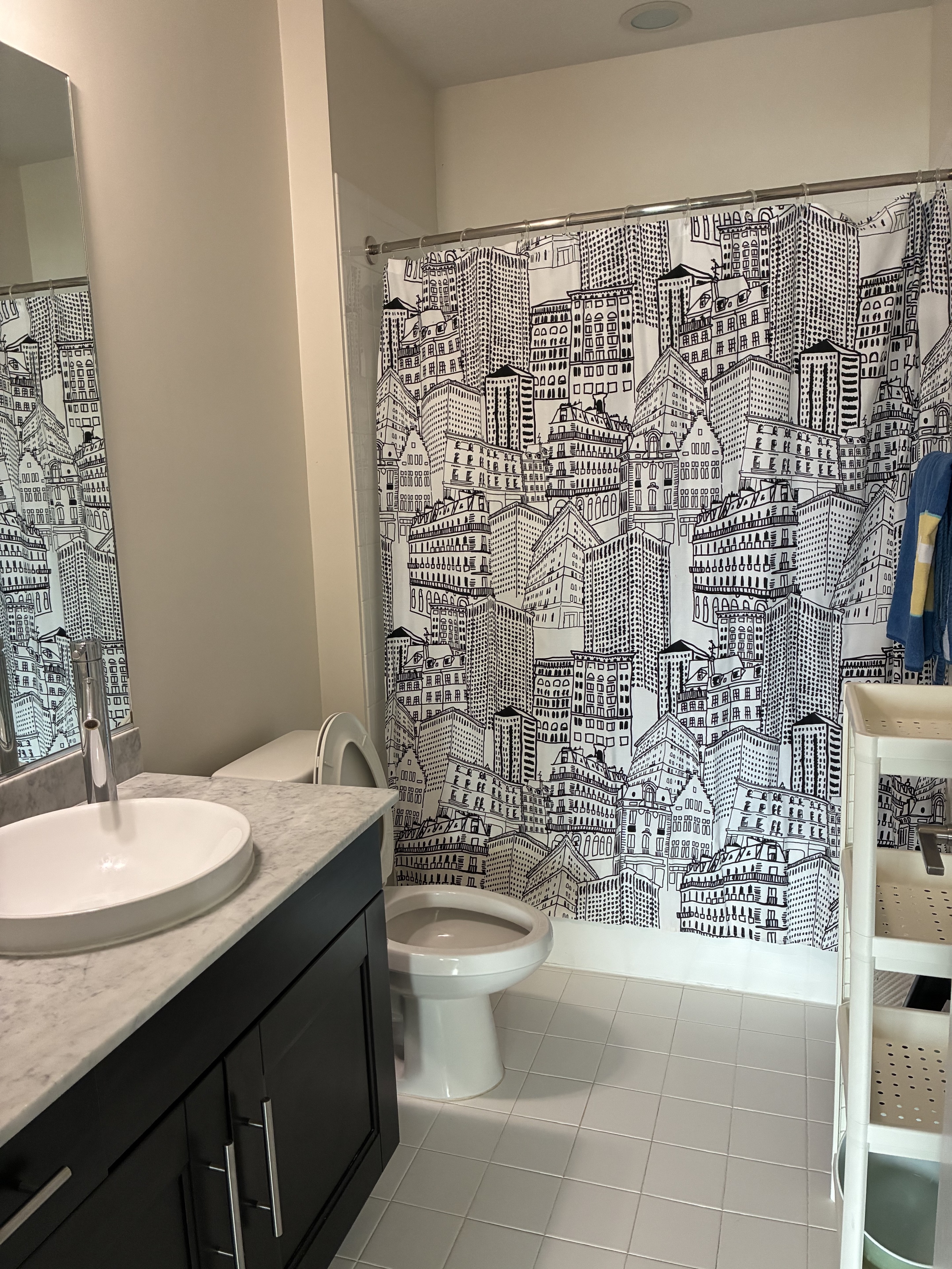Clean bathroom with vanity, toilet, tub, and patterned shower curtain