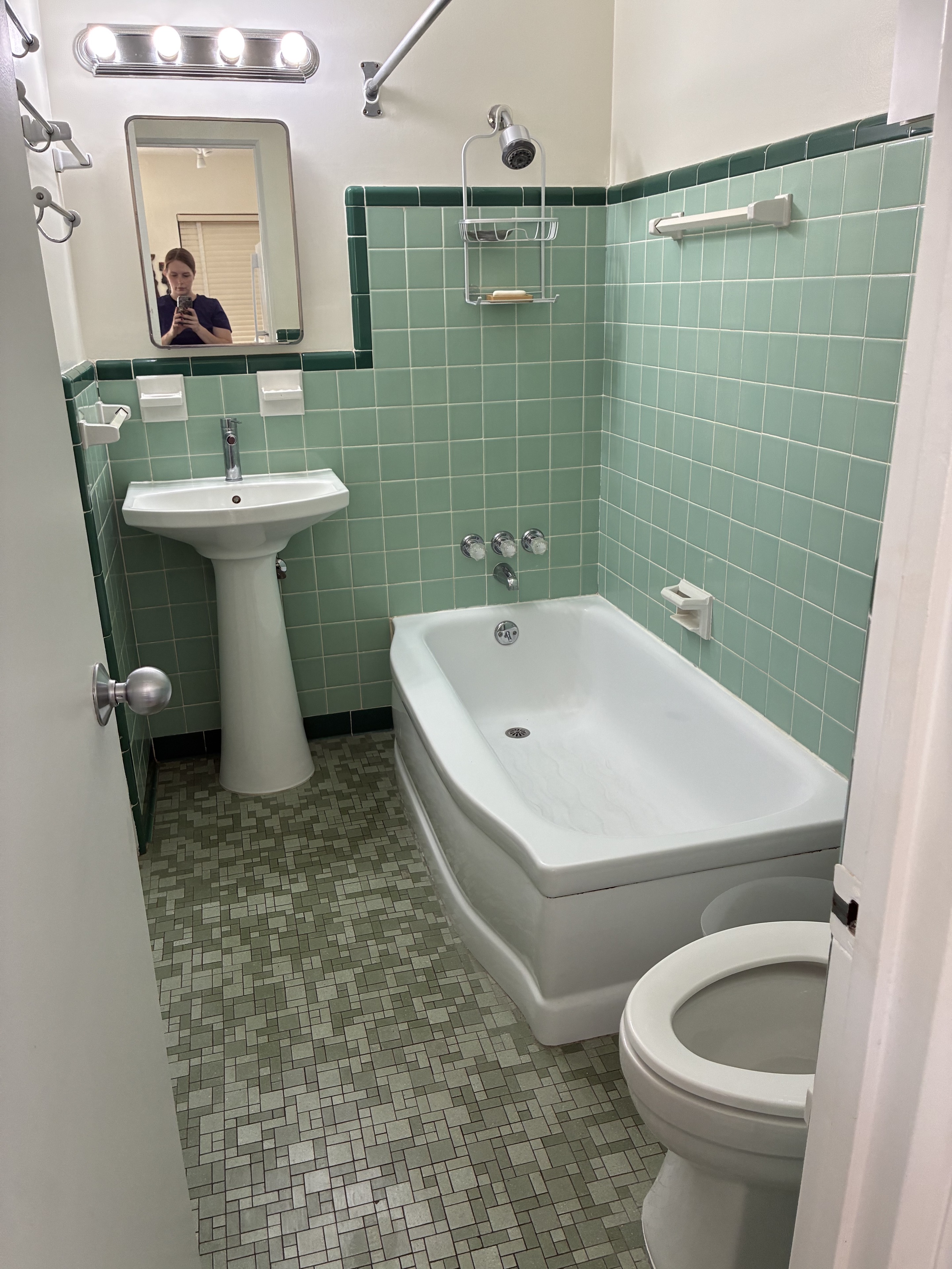 Clean vintage bathroom with green tile, tub, sink, and floor