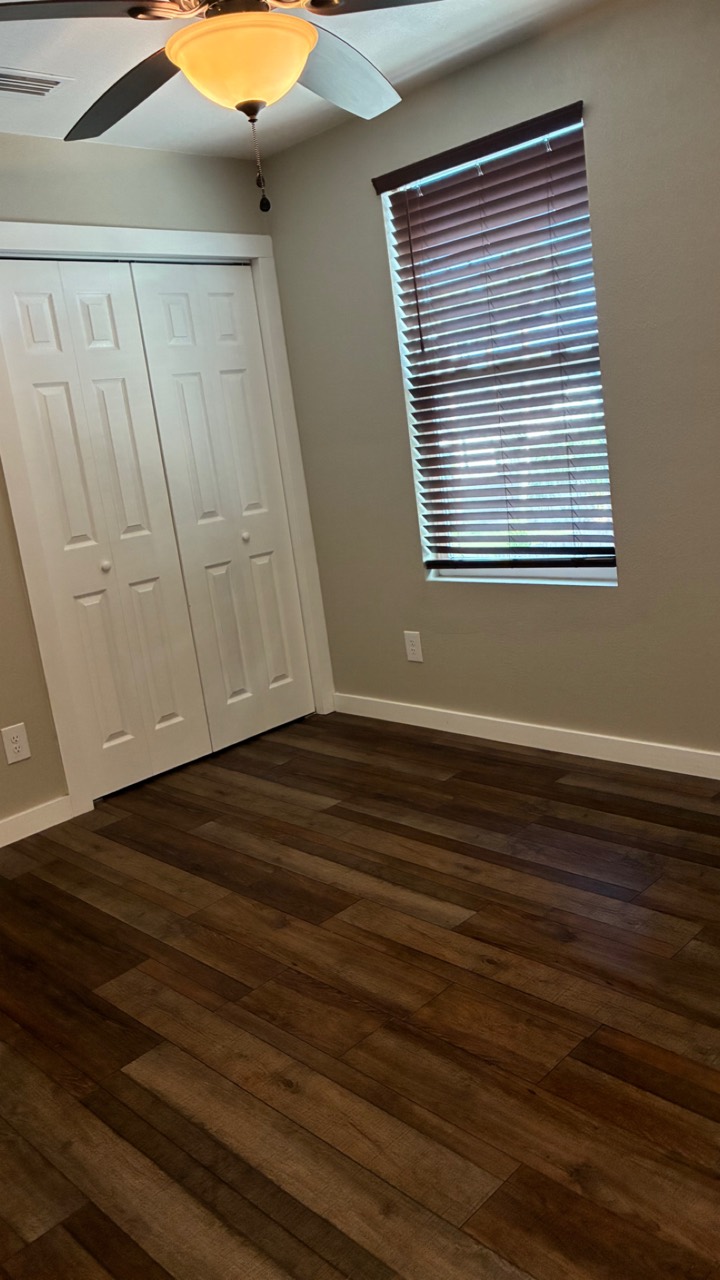 Clean bedroom with wood-look flooring, blinds, and closet doors