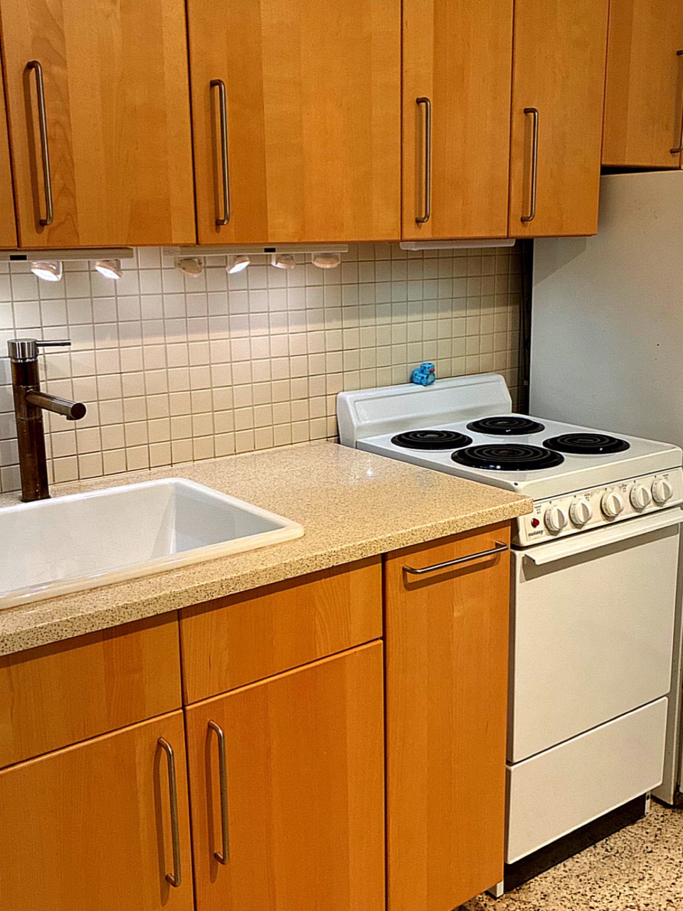 Clean compact kitchen with sink, stove, tile backsplash, and cabinets