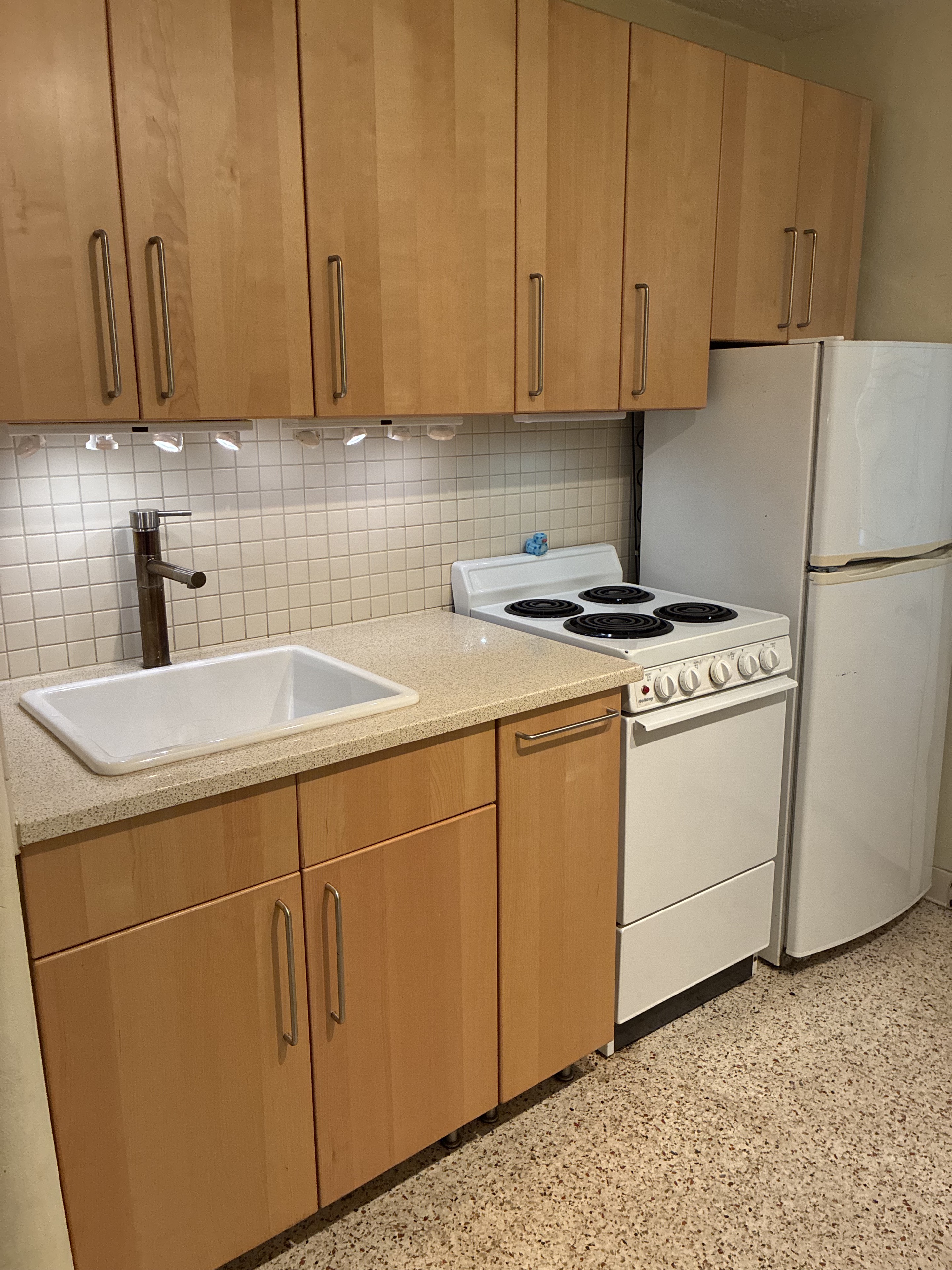 Clean compact kitchen with cabinets, sink, stove, and refrigerator