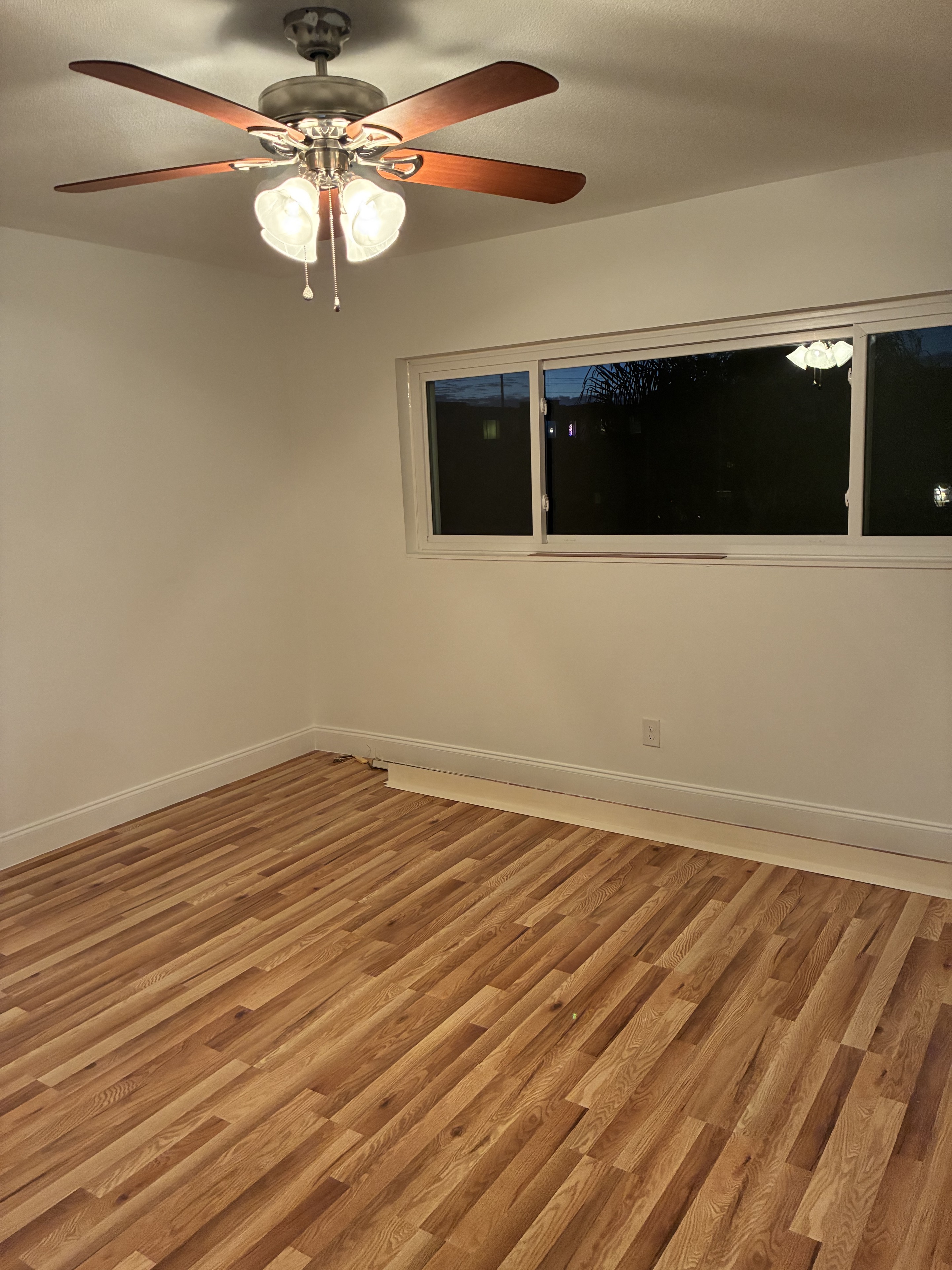 Clean empty bedroom with light hardwood floor, window, and ceiling fan