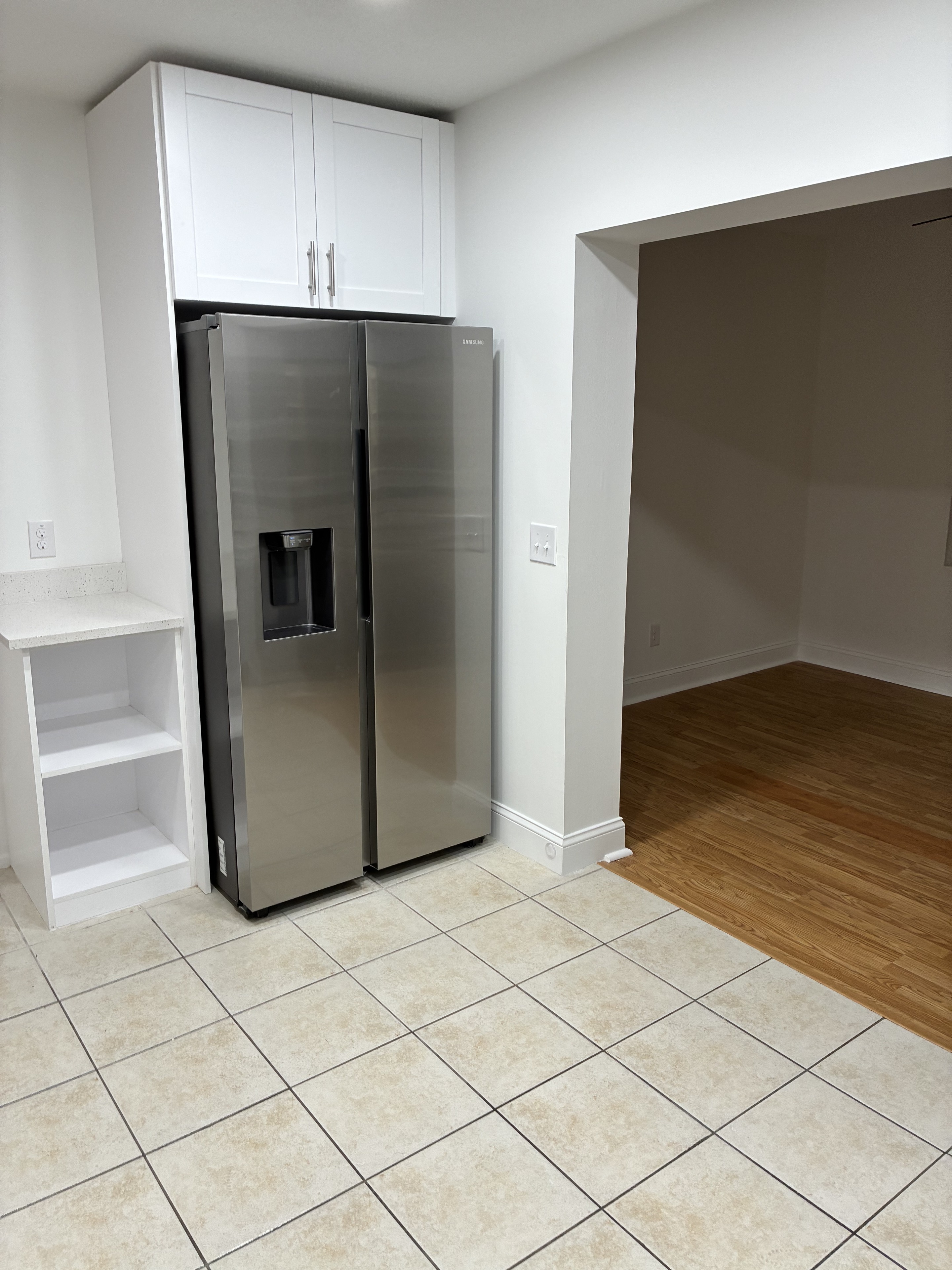 Clean stainless refrigerator area with tile floor and white cabinetry