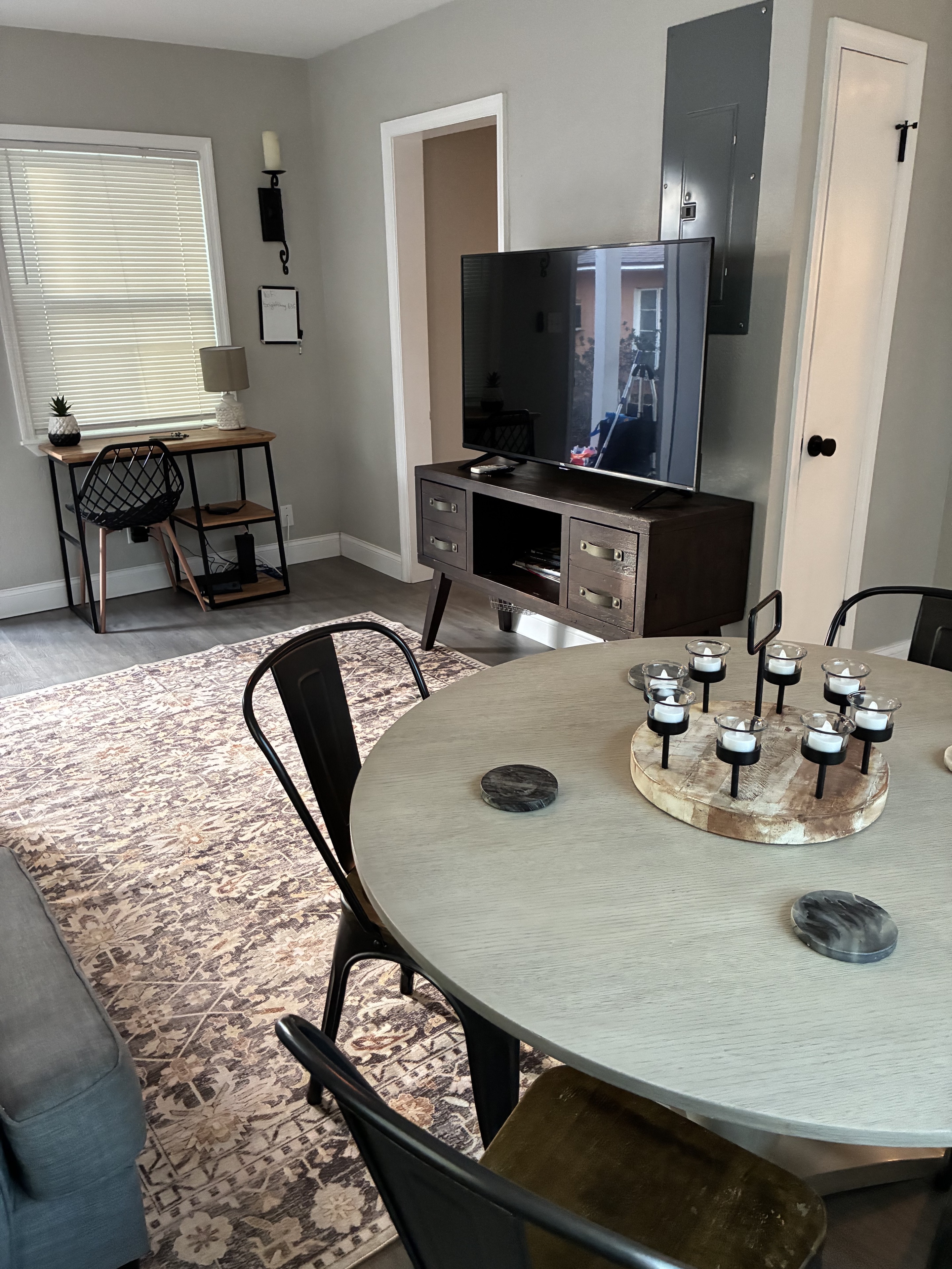 Clean furnished living and dining area with desk, TV, rug, and table