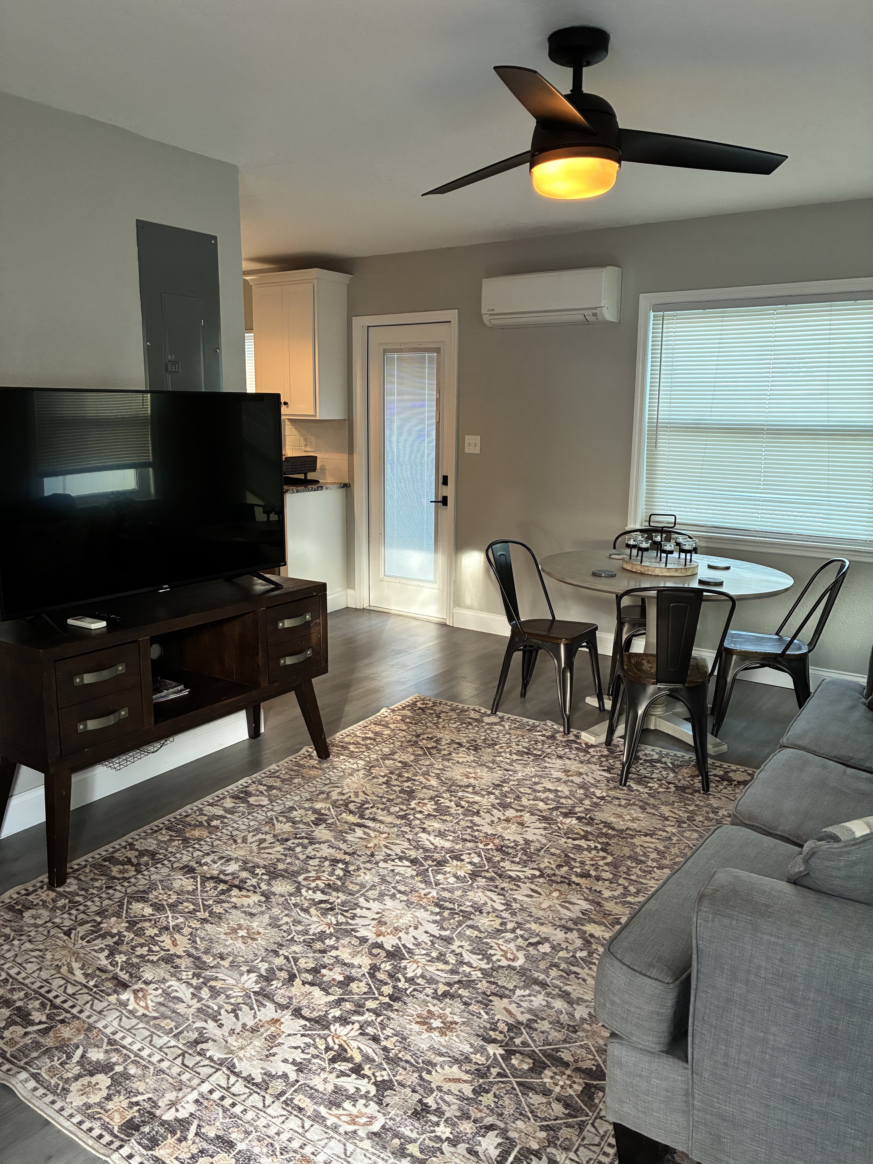 Clean furnished living room with dining table, sofa, TV, and rug