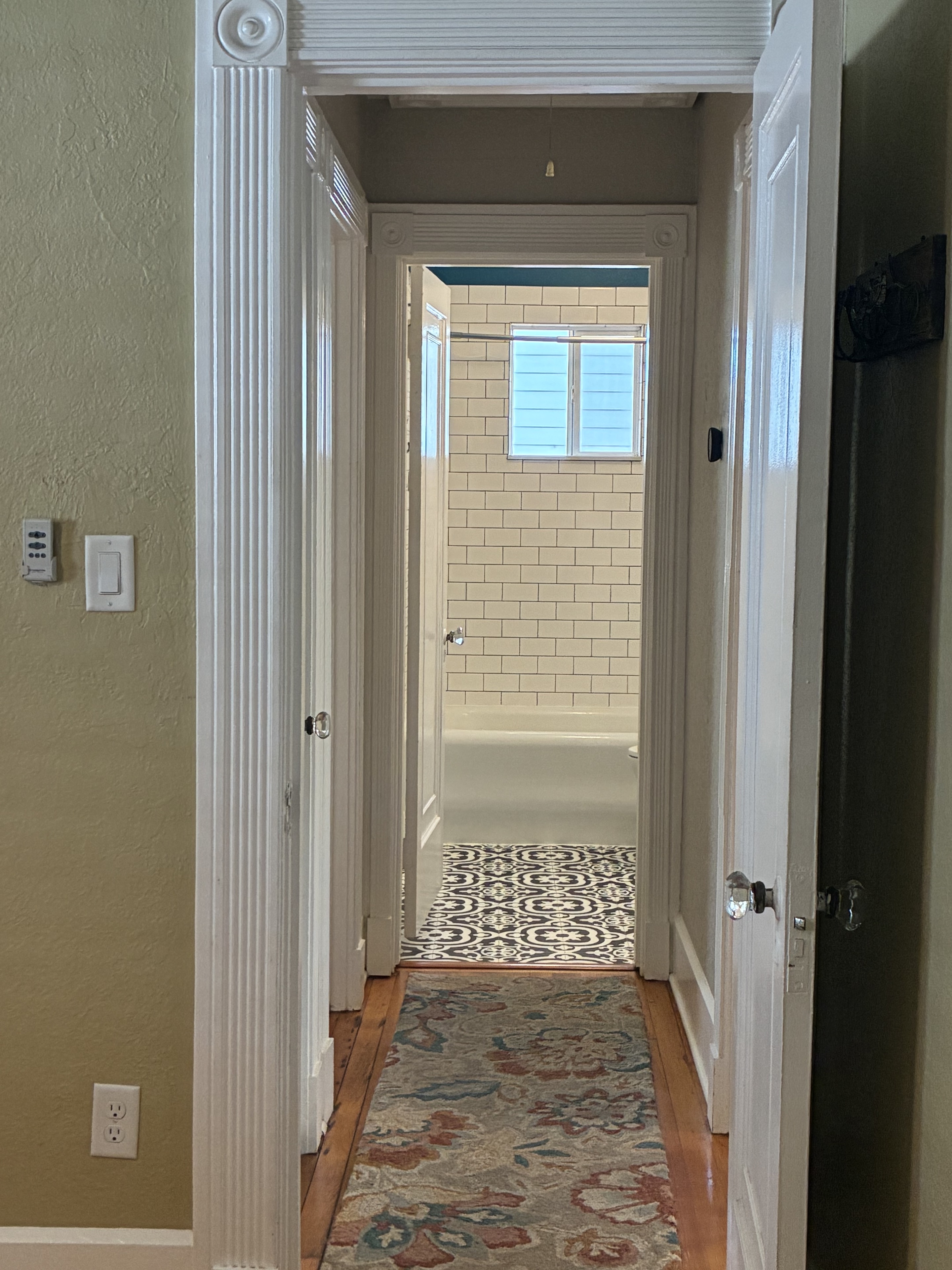 Clean hallway leading to bathroom with detailed trim and hardwood floor