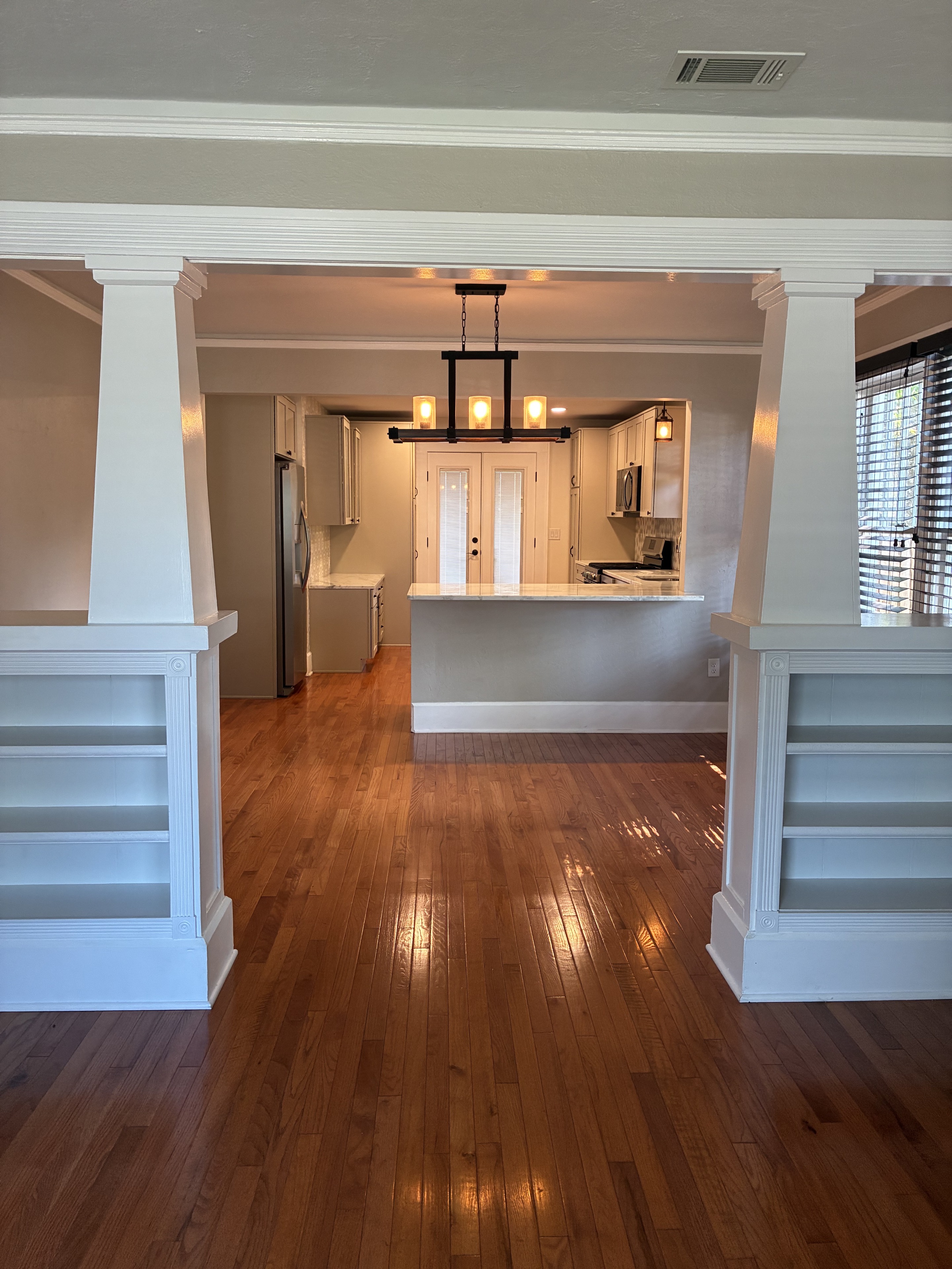 Clean hardwood floor leading into kitchen through white columns