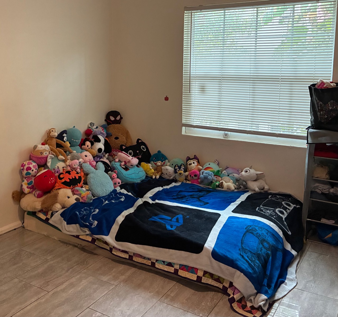 Kids bedroom reset with bed, window blinds, tile floor, and stuffed animals arranged along the wall