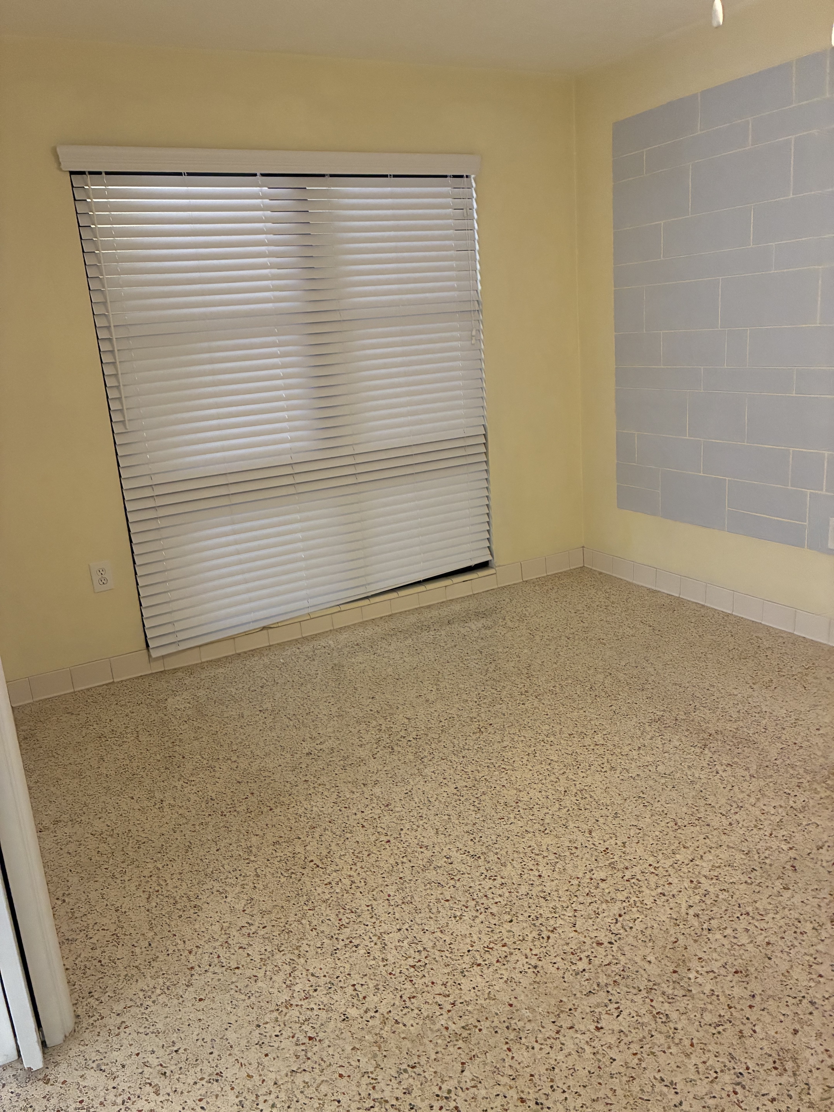 Clean room with blinds, tiled accent wall, and terrazzo floor