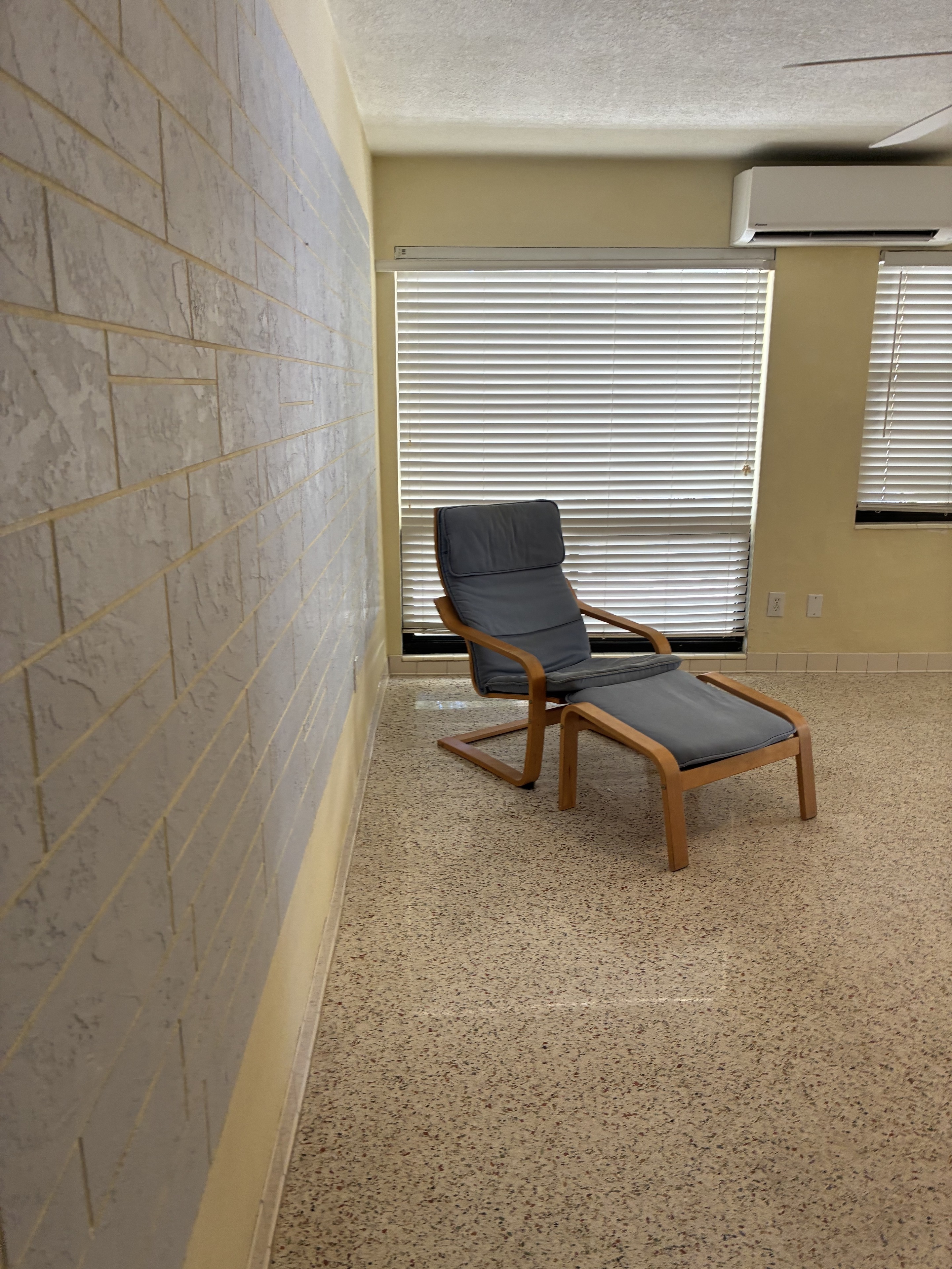 Clean terrazzo room with chair, blinds, and polished floor