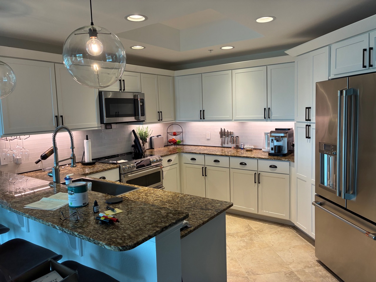 Clean white kitchen with granite counters, stainless refrigerator, and under-cabinet lighting