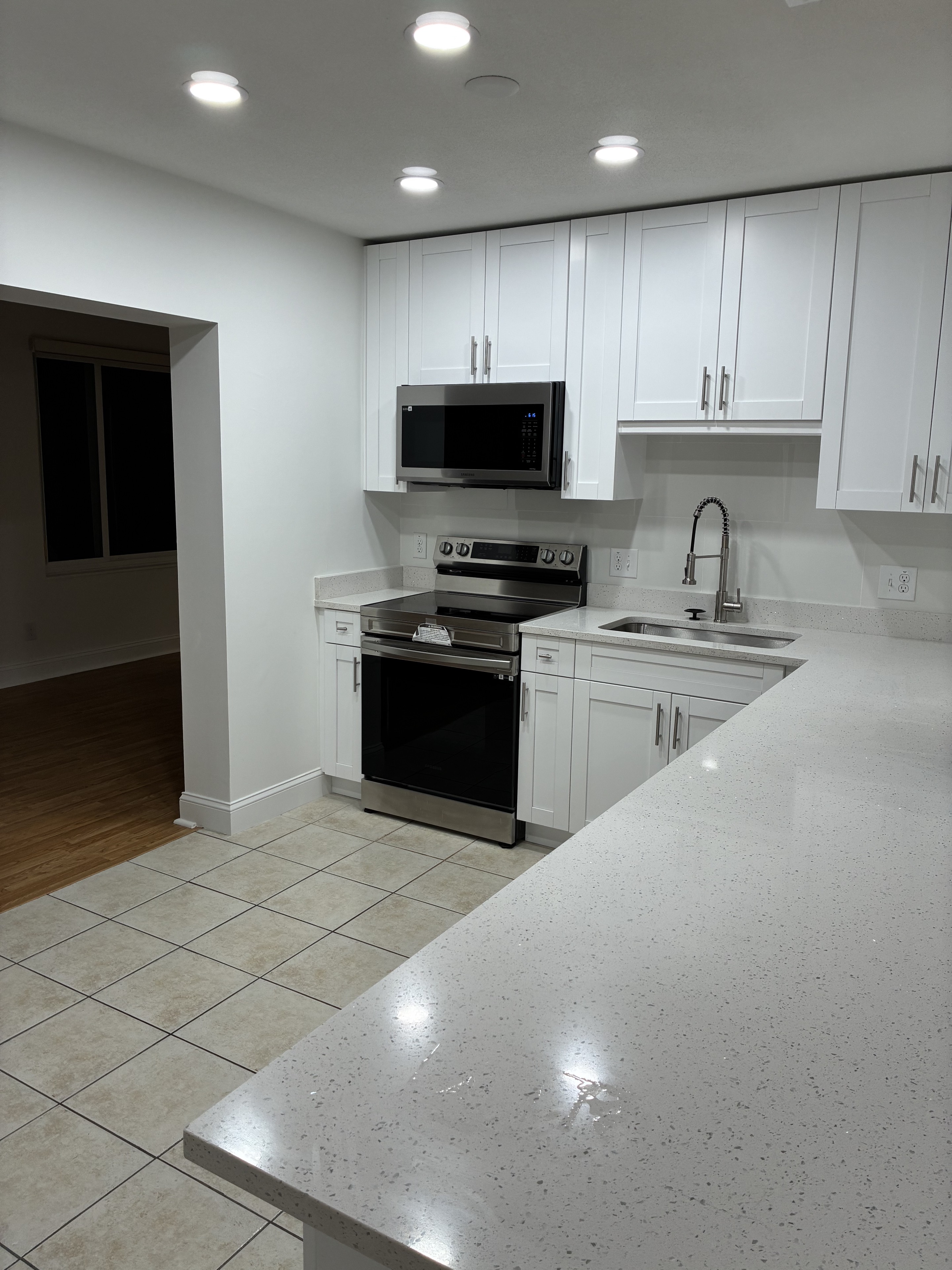 Clean white kitchen with stainless appliances, tile floor, and bright counters